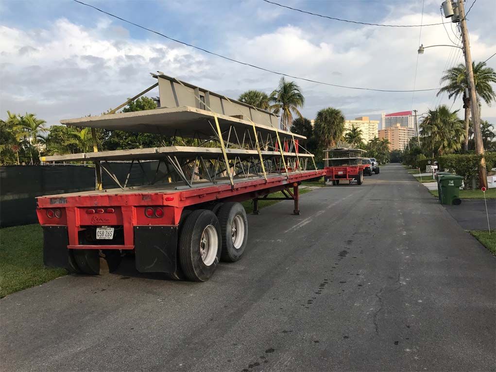 A red semi truck is carrying a stack of concrete slabs down a street.
