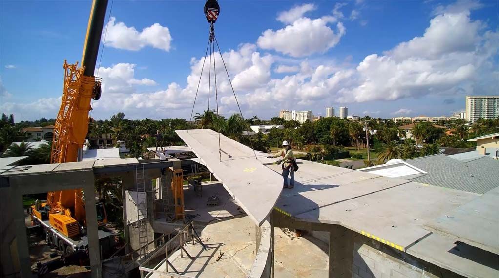 A crane is lifting a piece of concrete on top of a building.