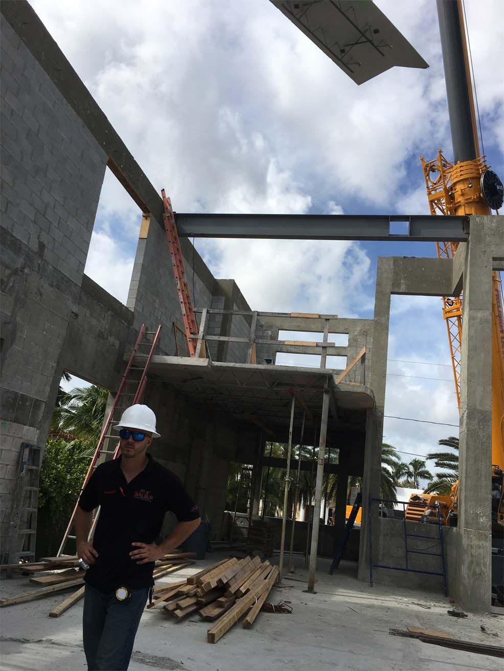 A man wearing a hard hat is standing in front of a building under construction.