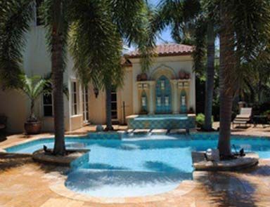 A large swimming pool surrounded by palm trees in front of a house