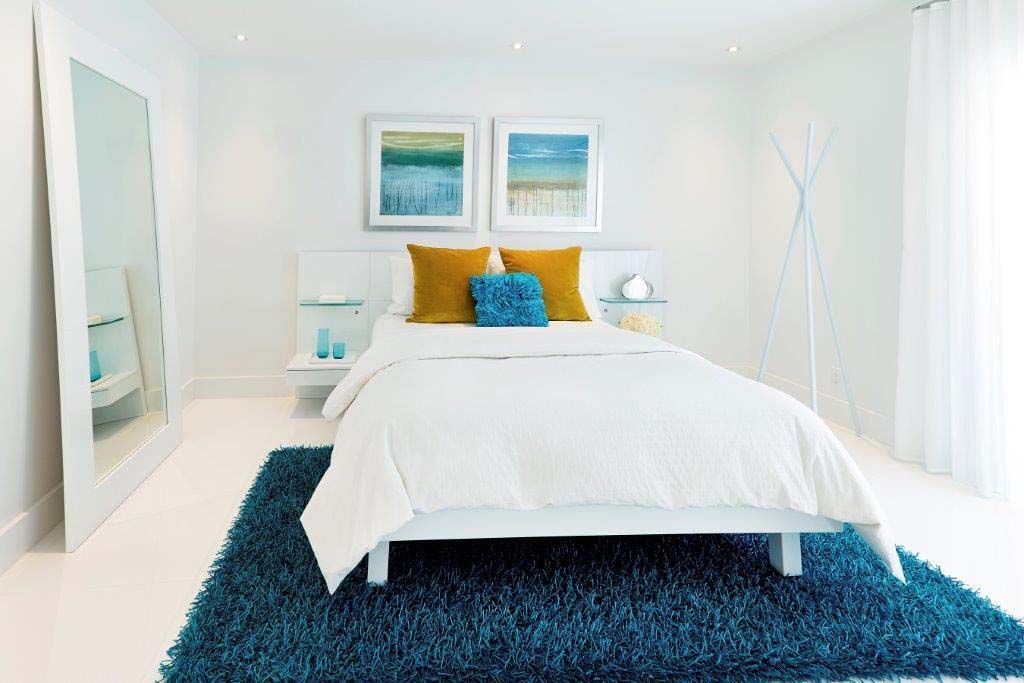 A bedroom with a white bed and a blue rug.