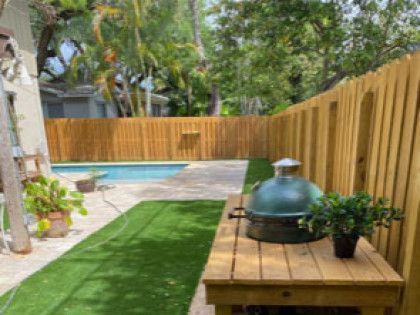 A wooden table with a grill on it in a backyard next to a pool.