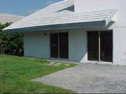 A white house with a lot of windows and a roof is sitting on top of a lush green field.