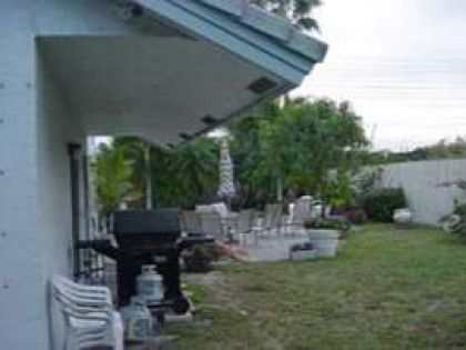 A backyard with a grill , chairs , umbrellas and a pool.