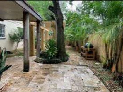A patio with a covered walkway leading to a house surrounded by trees and bushes.
