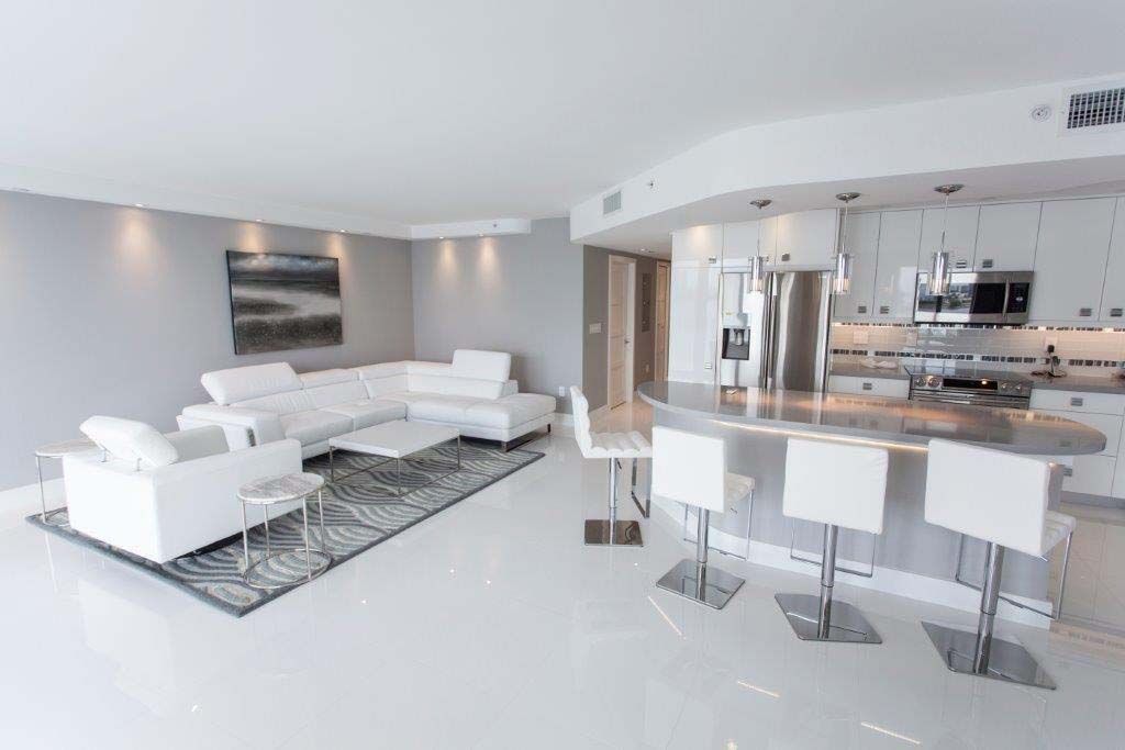 A living room and kitchen in a house with white furniture.