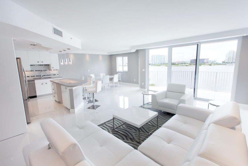 A living room with a white couch , chair , coffee table , and kitchen.