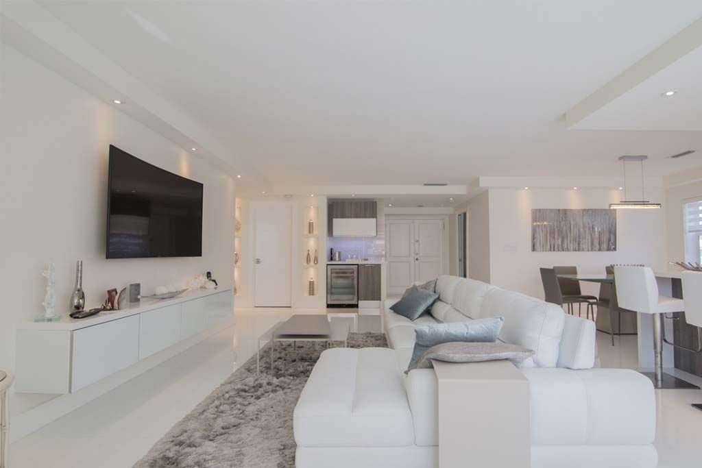 A living room with a white couch and a flat screen tv on the wall.