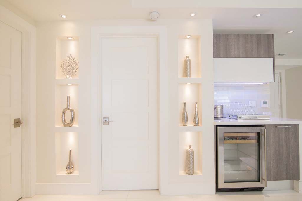 A living room with a door , shelves , and a refrigerator.