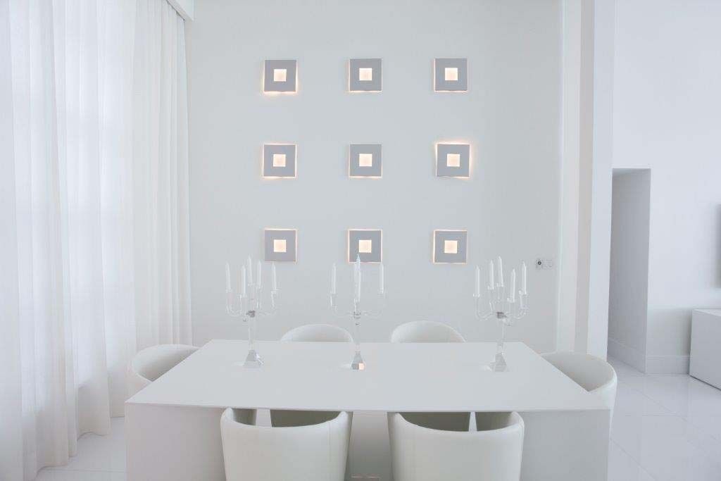A dining room with a table and chairs and a white wall.