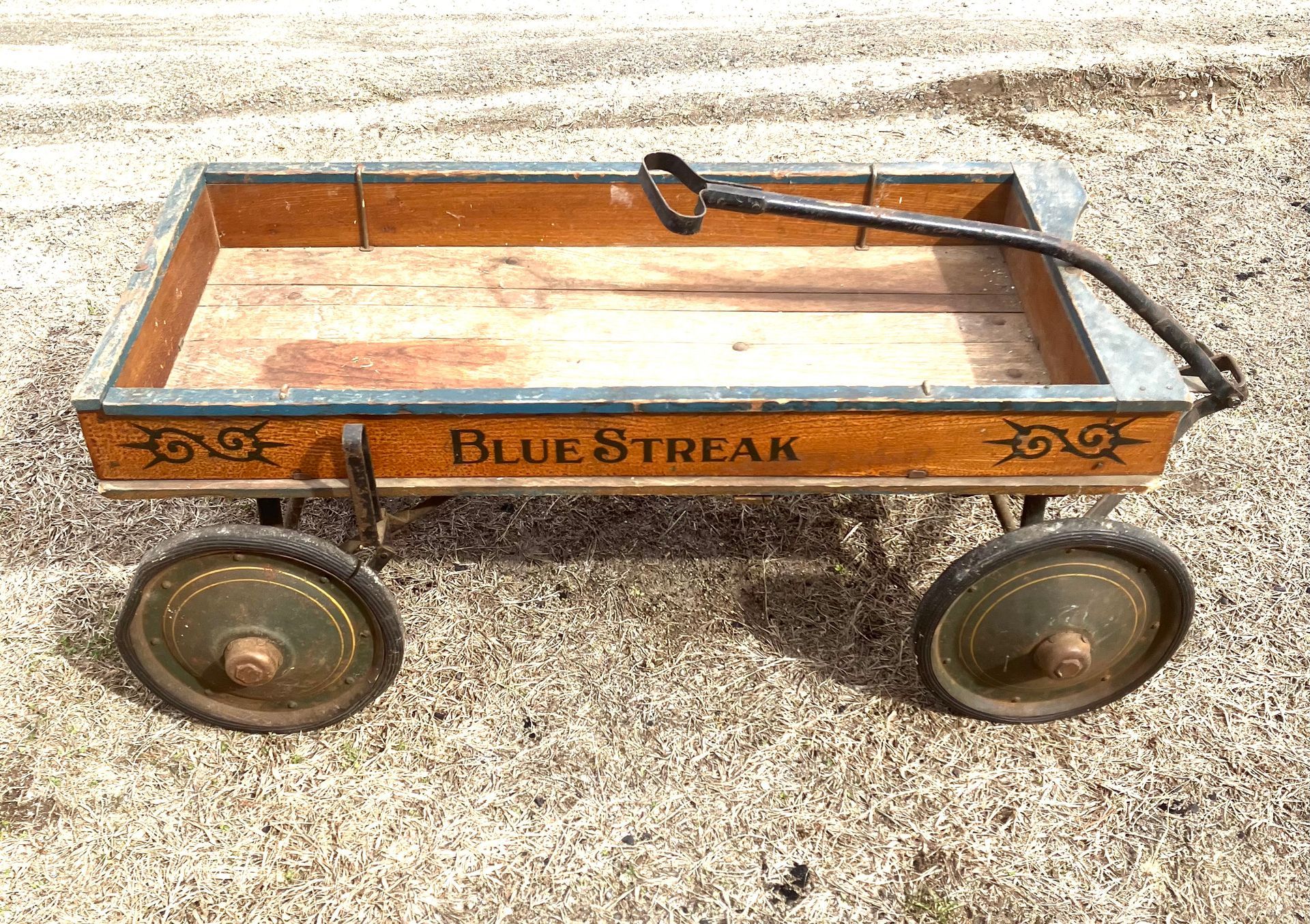 Rustic wooden wagon with four wheels and Blue Streak lettering on a gravel surface