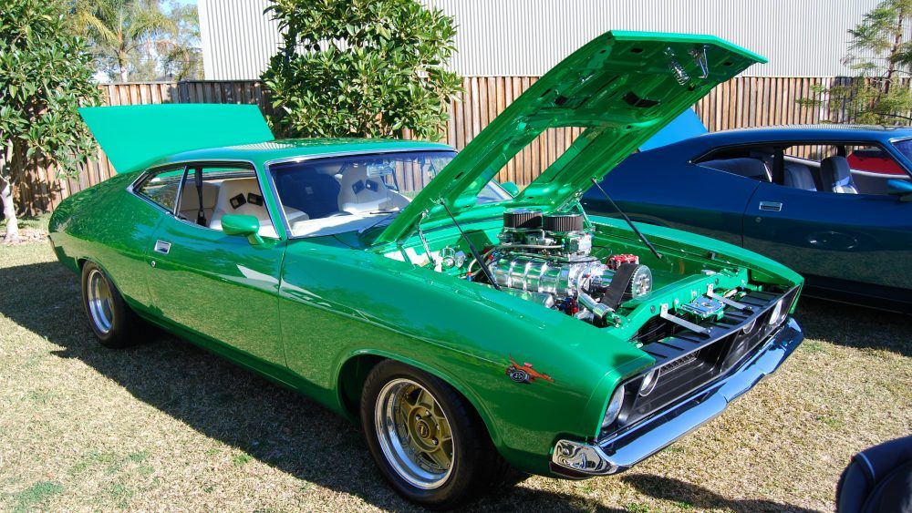 a green Ford classic muscle car with its hood open