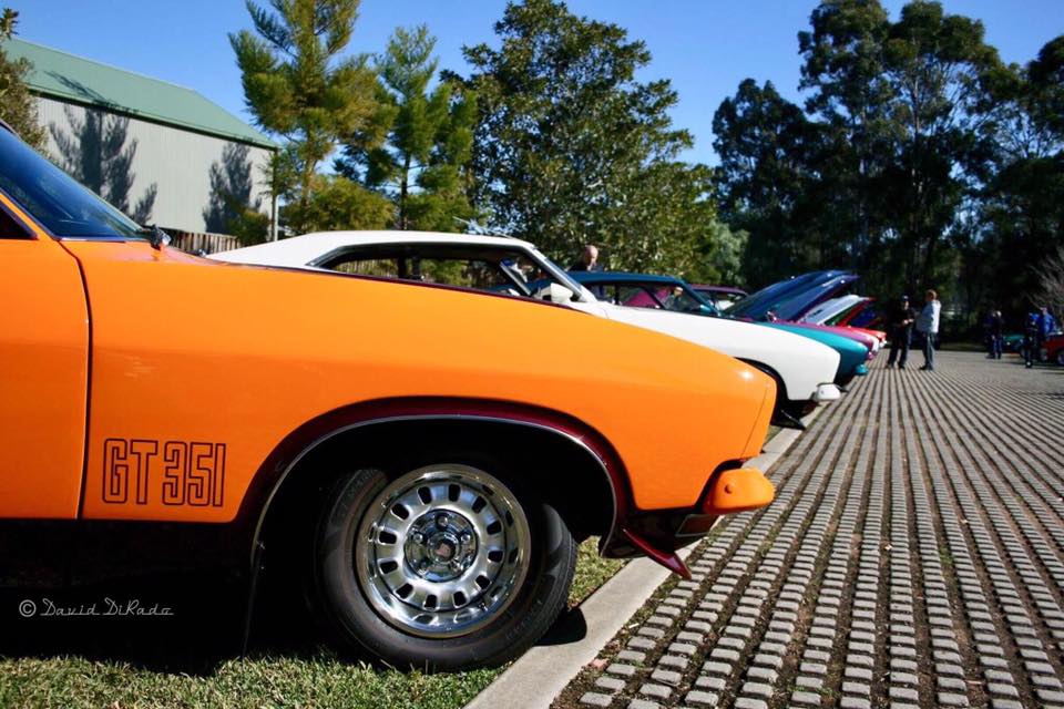orange Ford classic muscle car with other muscle cars behind it