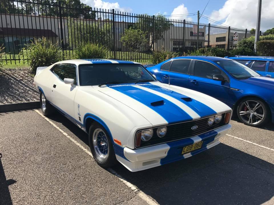 a white Ford classic muscle car with blue stirpes