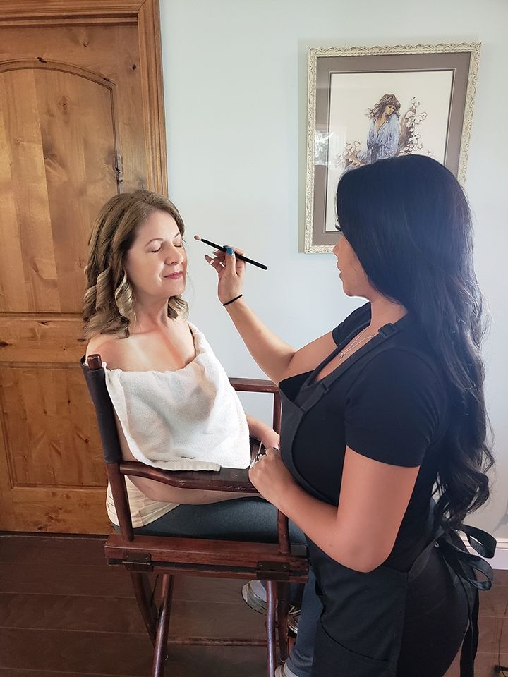 A woman is applying makeup to another woman while sitting in a chair.