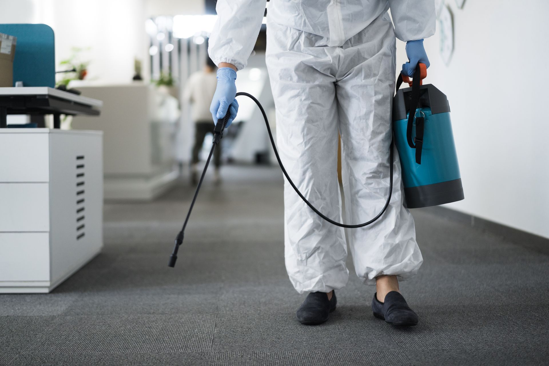 Person wearing protective suit spraying office floor for pest control.