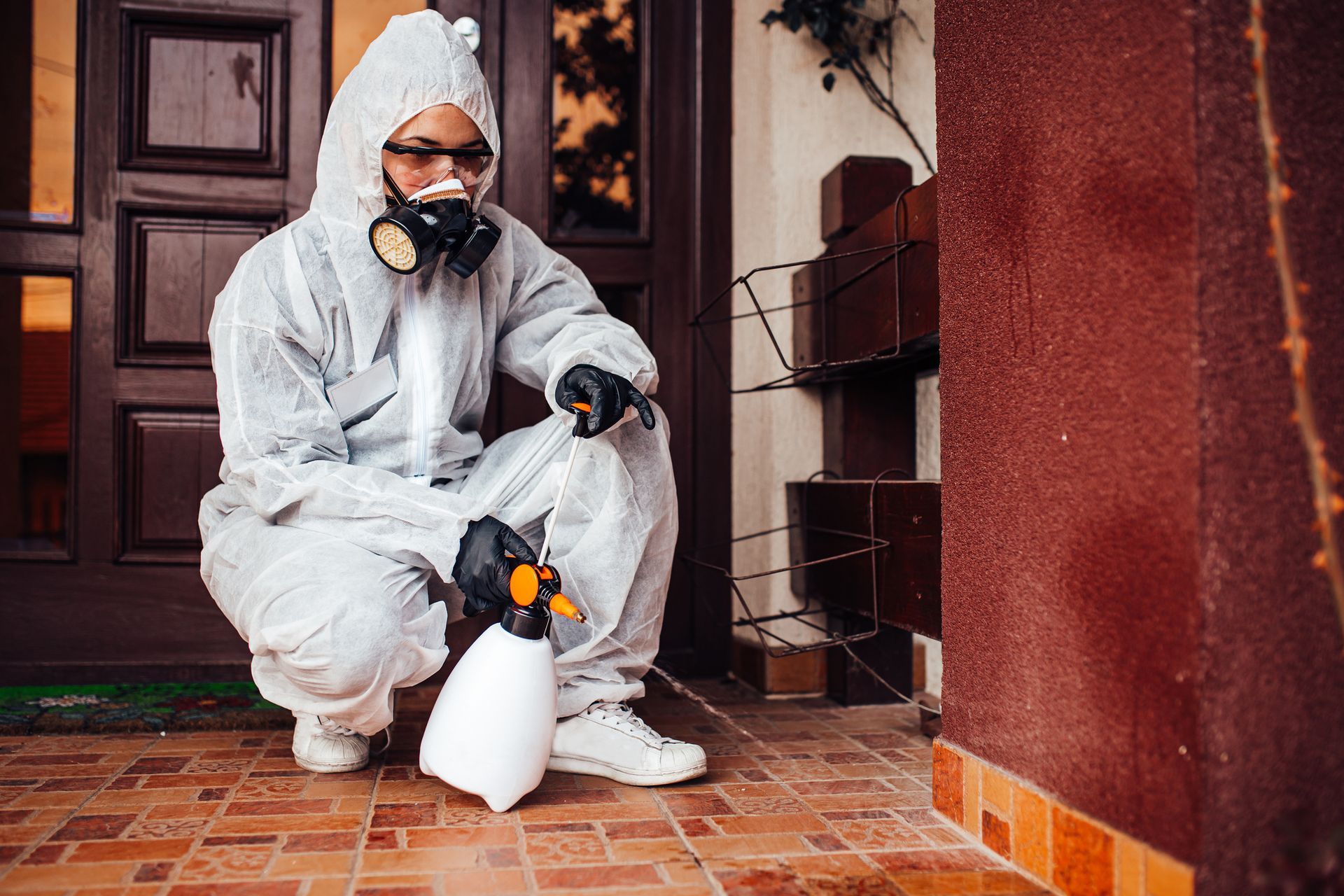 Person in protective suit spraying disinfectant on tiled floor near a doorway.
