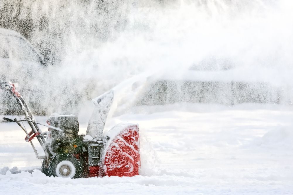 A snow blower is blowing snow in a driveway.