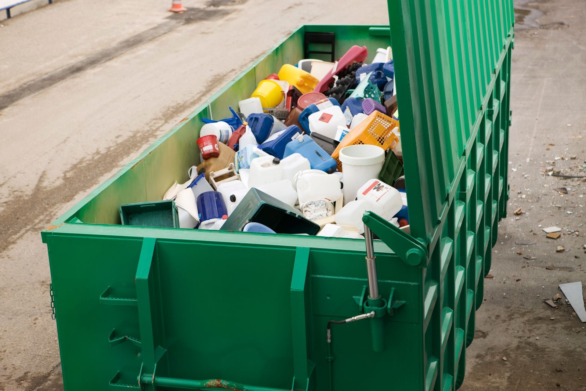 A green dumpster filled with plastic bottles and containers.