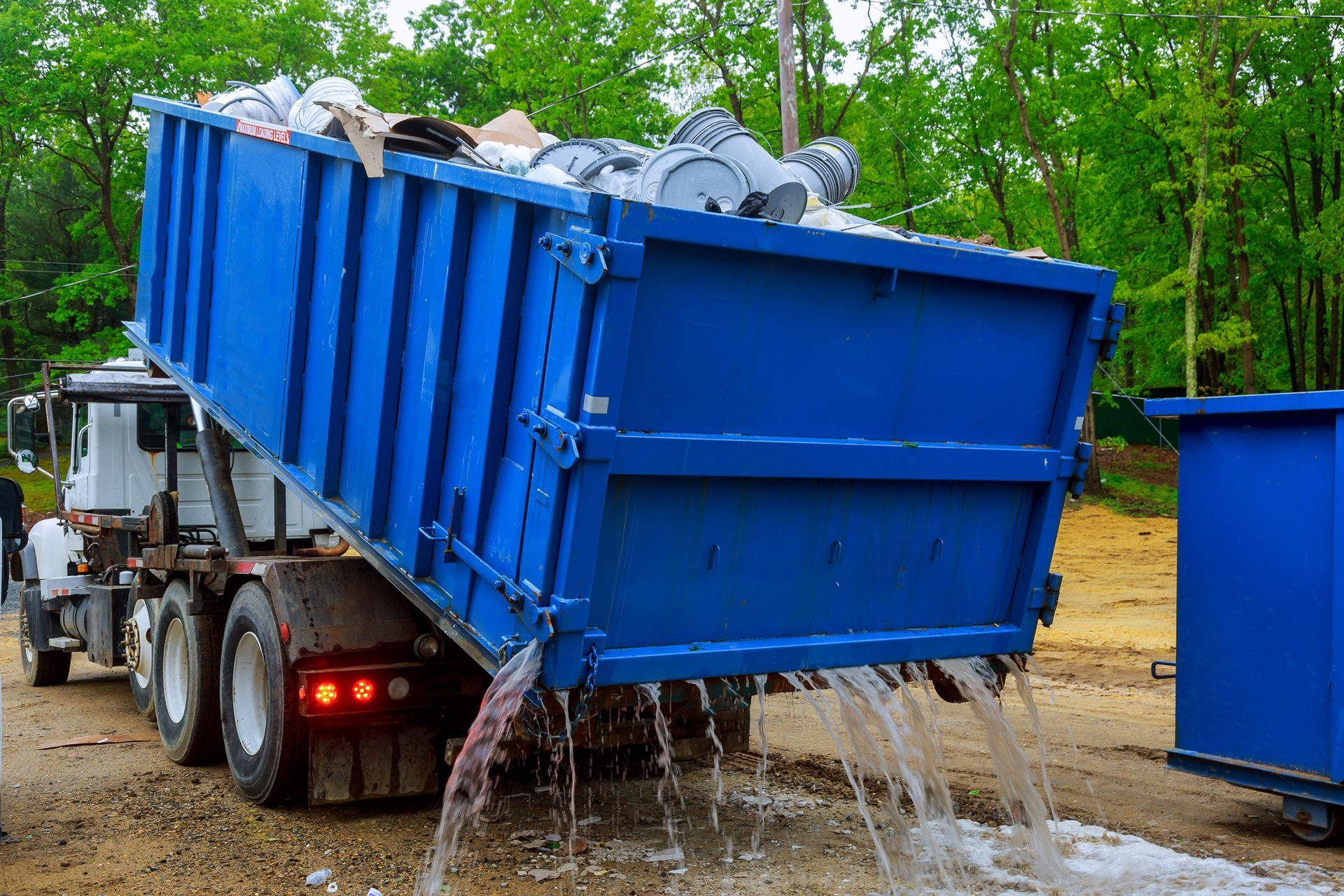 A dumpster truck is being filled with trash and water is pouring out of it.