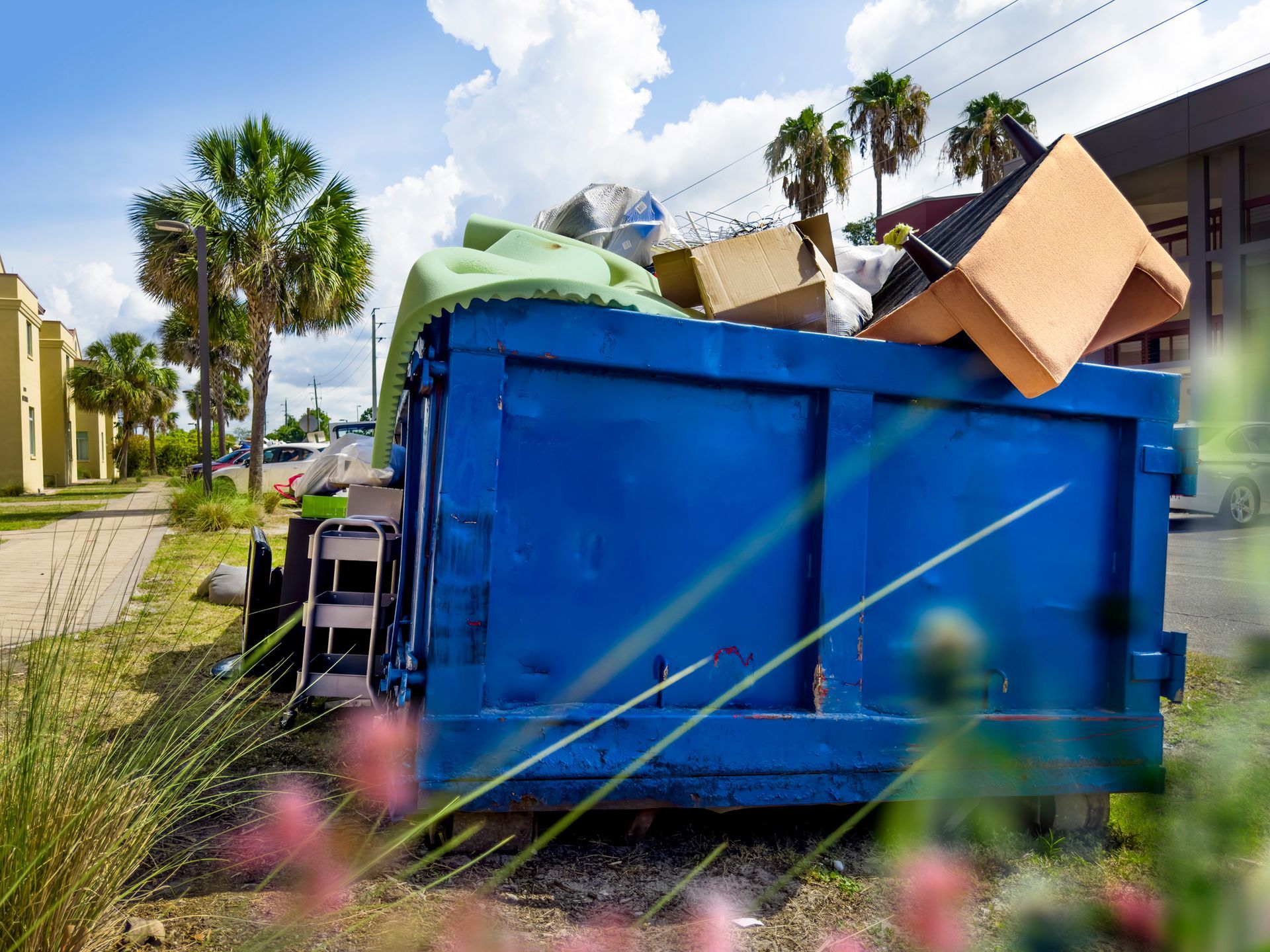 A blue dumpster filled with boxes is sitting on the side of the road.