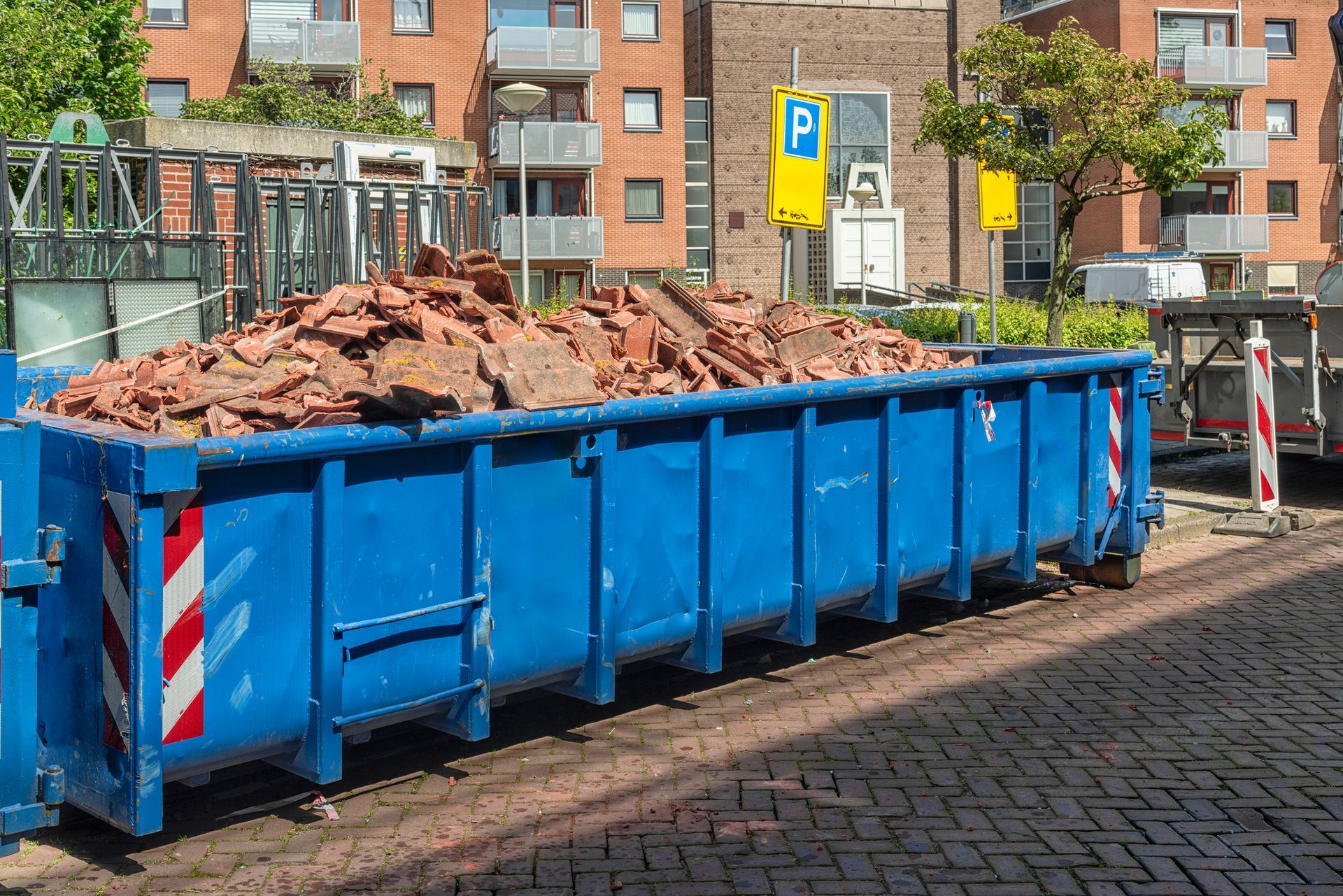 A blue dumpster filled with bricks is parked on the side of the road.