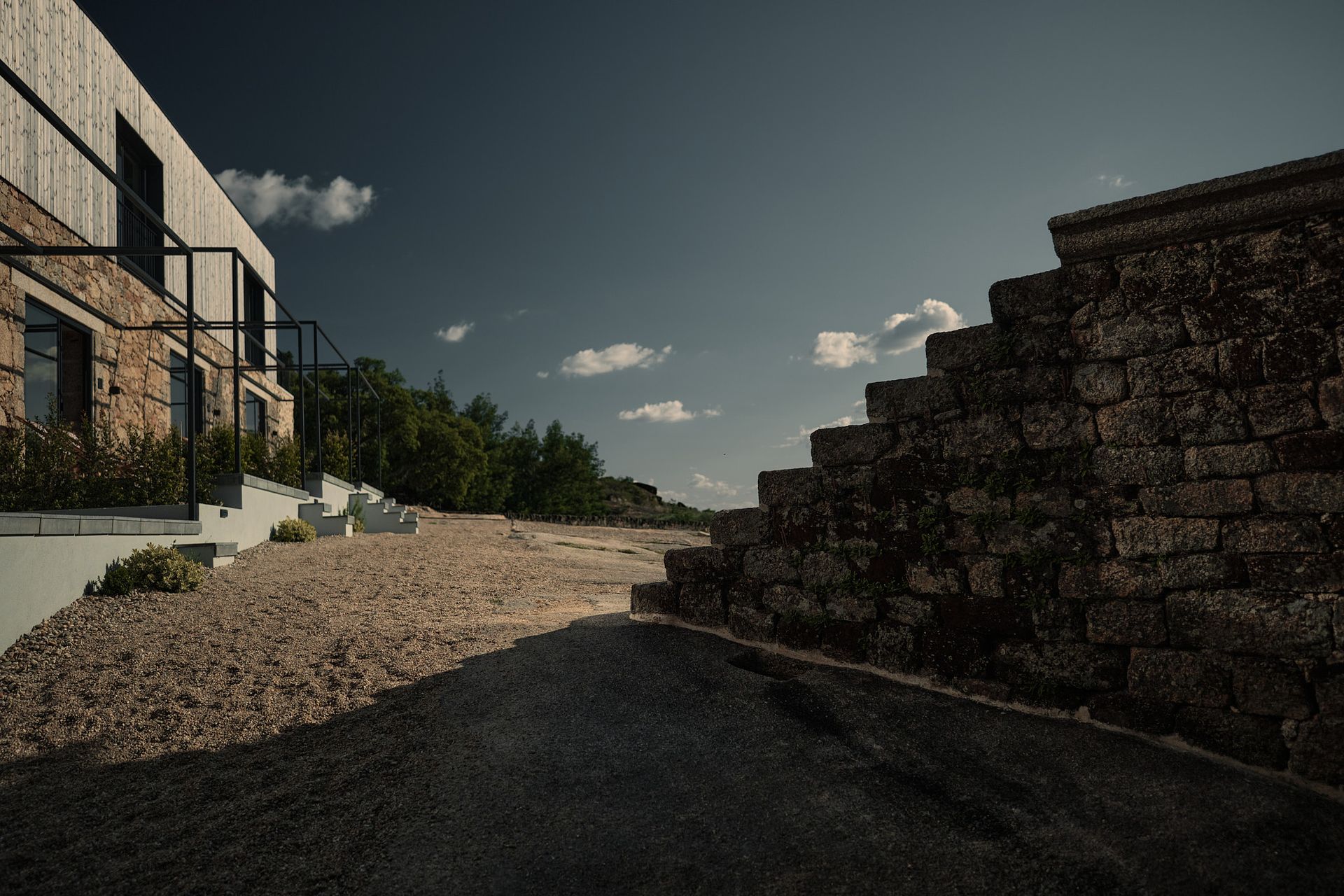 A road leading to a building with a stone wall in the background.