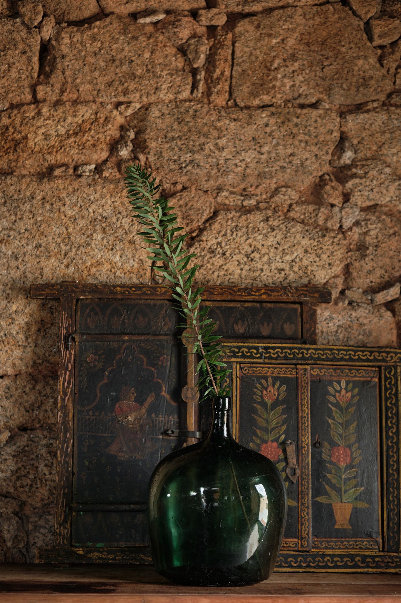 A green vase with a plant in it is sitting on a wooden table.