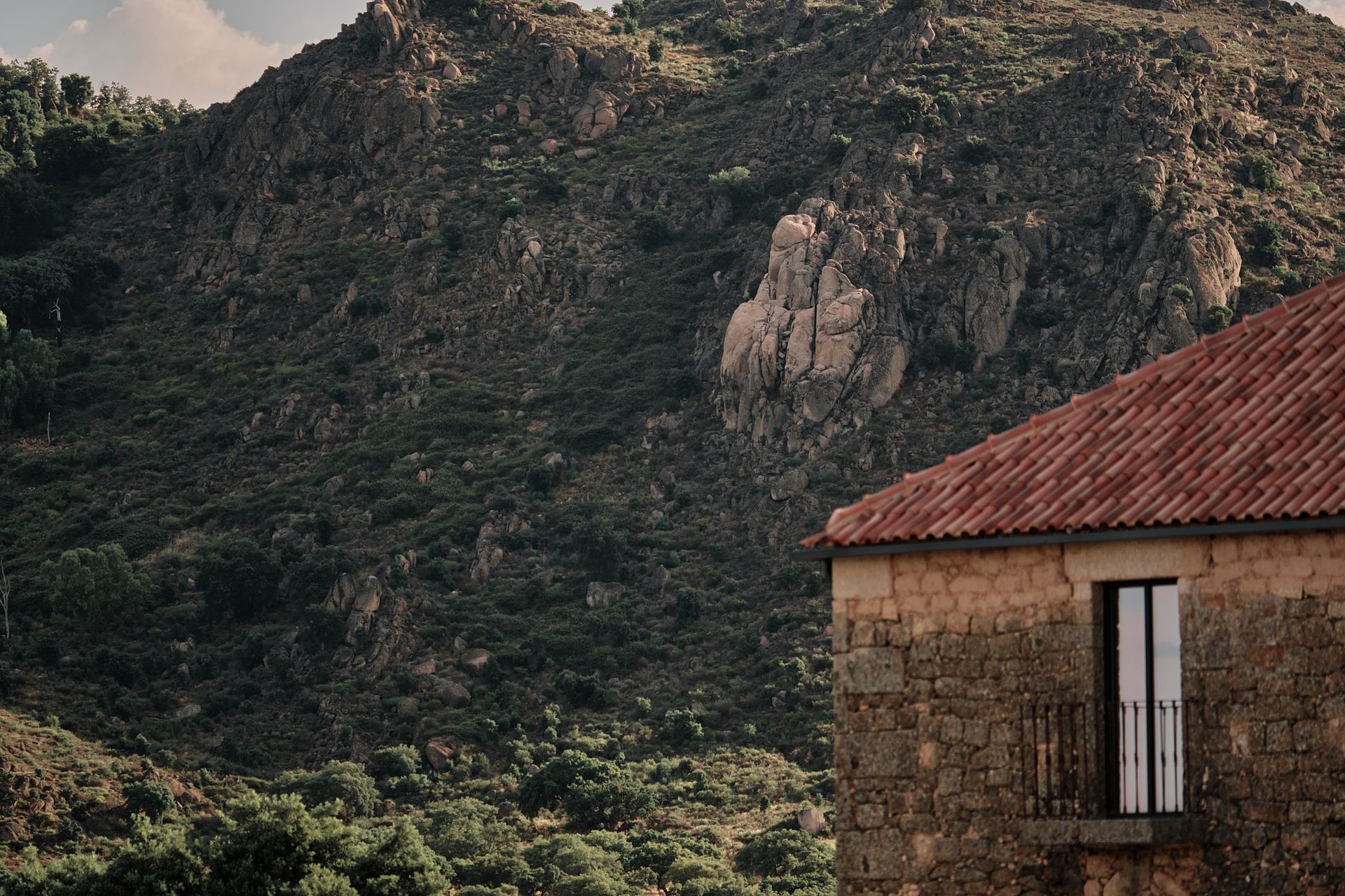 A stone house with a red tiled roof is sitting in front of a mountain.