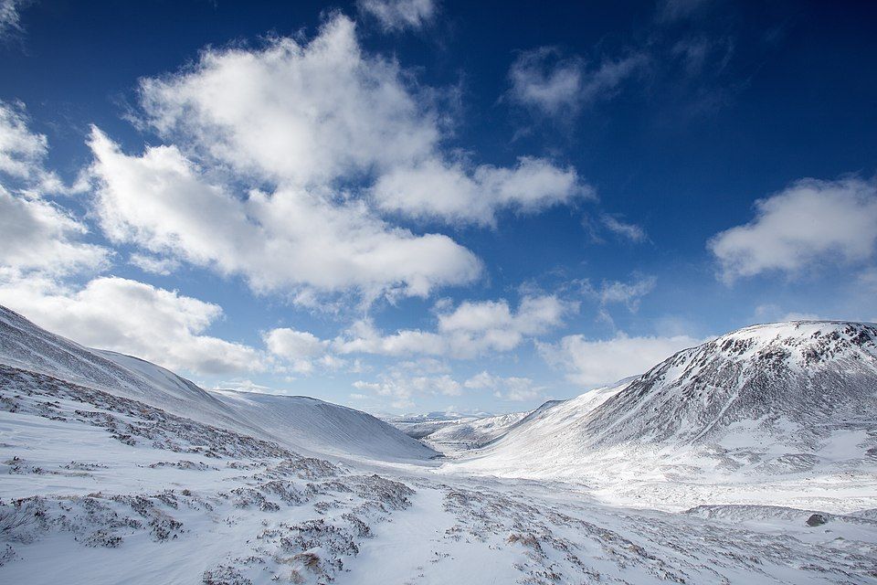 The Cairngorm mountains in the Highlands of Scotland under a blue sky with white clourd and covered in snow