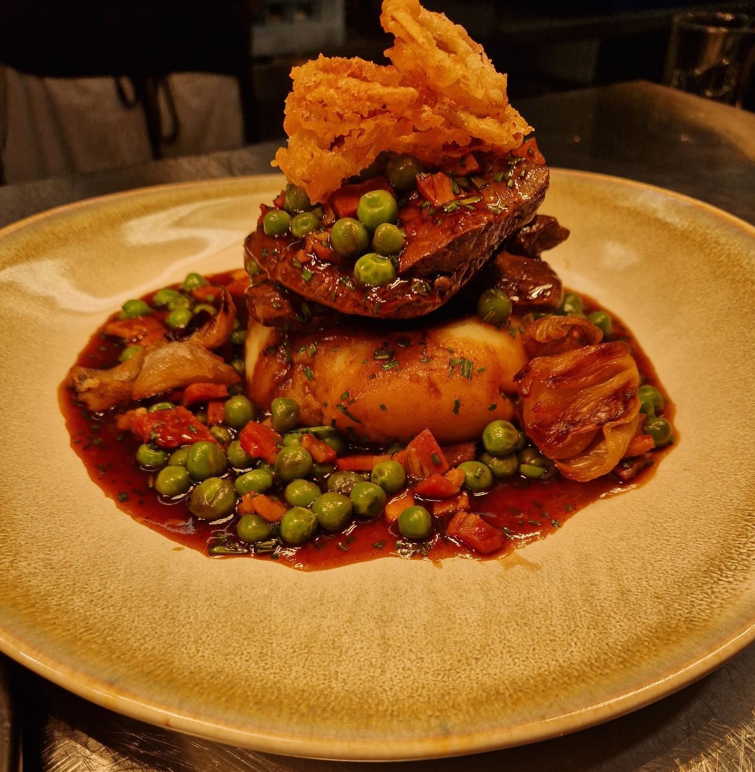 A close-up view of Lamb's liver and peas with bacon and crispy onions