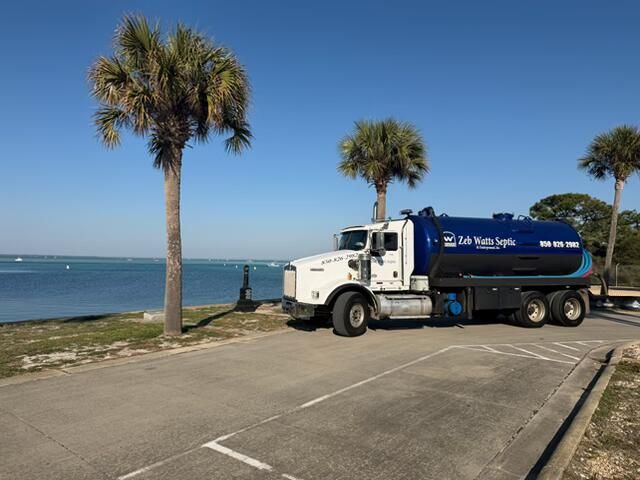 Blue water tanker truck parked near a coast under palm trees on a sunny day.
