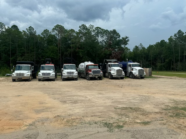 A row of trucks are parked in a dirt lot.