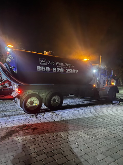 A large truck is parked on a brick sidewalk at night.