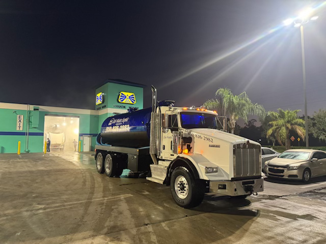A tanker truck is parked in a parking lot at night.