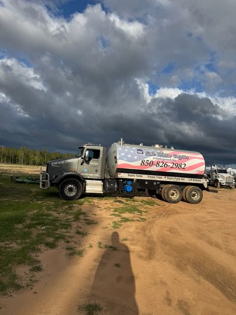 A tanker truck with an american flag on the side is parked in a dirt field.