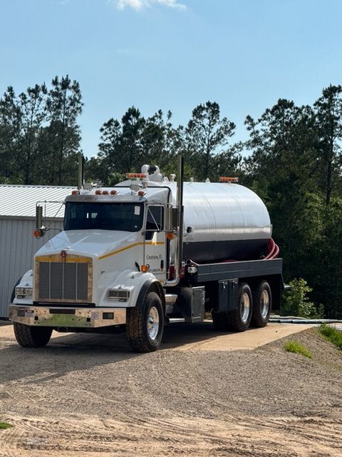 A white tanker truck is parked in a gravel lot.