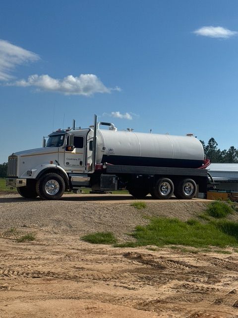 A white semi truck is parked on the side of a dirt road.