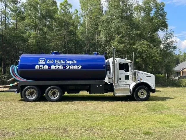 A blue and white septic truck is parked in a grassy field.