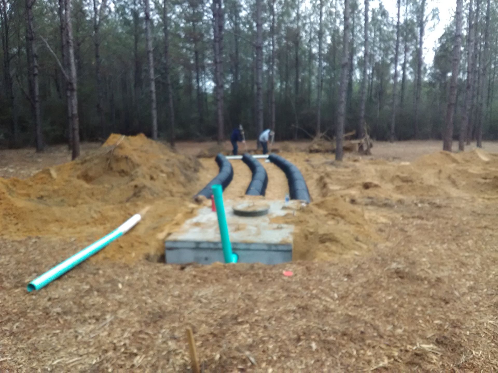 A blue excavator is digging a hole in the dirt in a field.