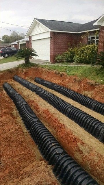 Black corrugated pipes laid in trenches in front of a brick house for drainage.