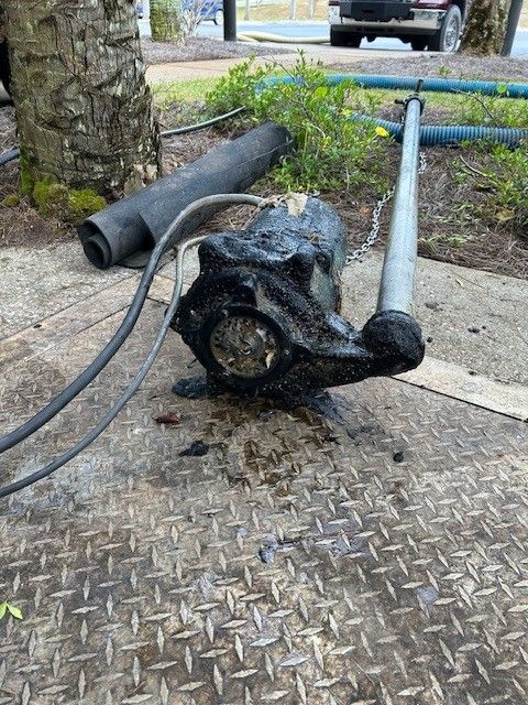A dirty, oil-covered water pump with connected tubes, lying on a metal surface, outdoors near vegetation.