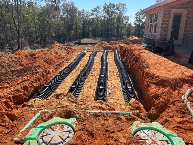 Four black septic drain lines in trenches, near a house under construction.