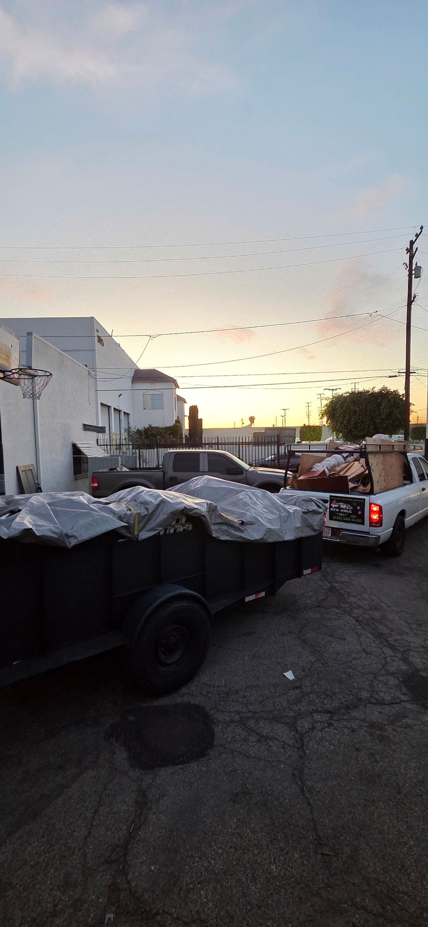 A white truck is towing a trailer in a parking lot at sunset.