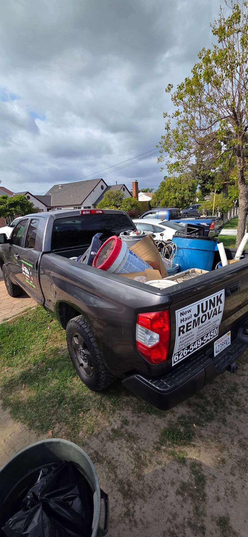 A truck is parked in a grassy area with a lot of trash in the back.