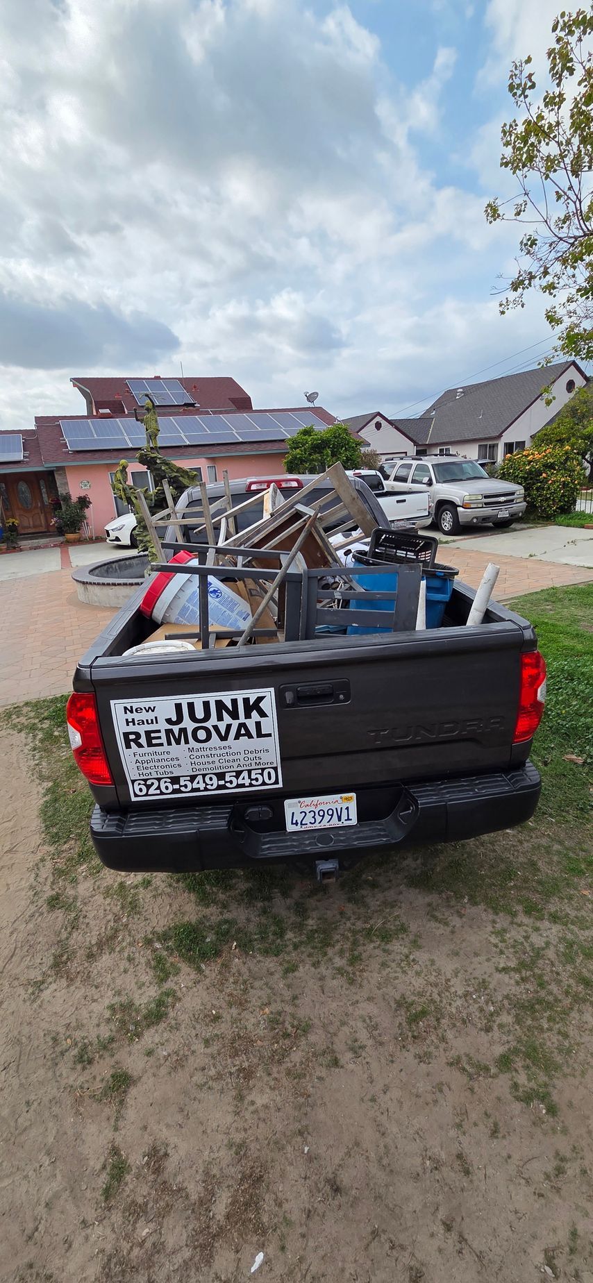 A junk removal truck is parked in the grass in front of a house.