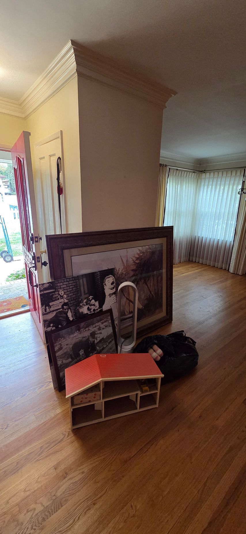 A doll house is sitting on the floor in a living room next to a picture.