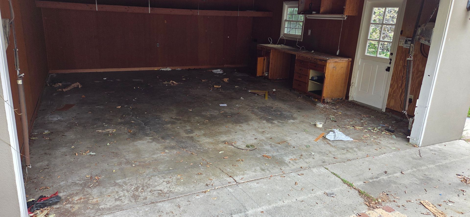 An empty garage with a concrete floor and a wooden door.