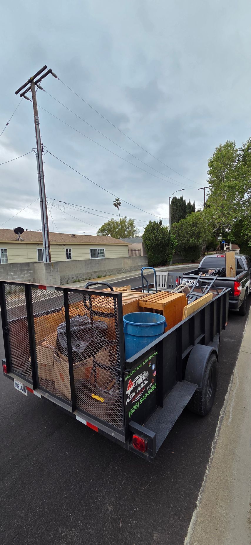 A trailer filled with lots of junk is parked on the side of the road.