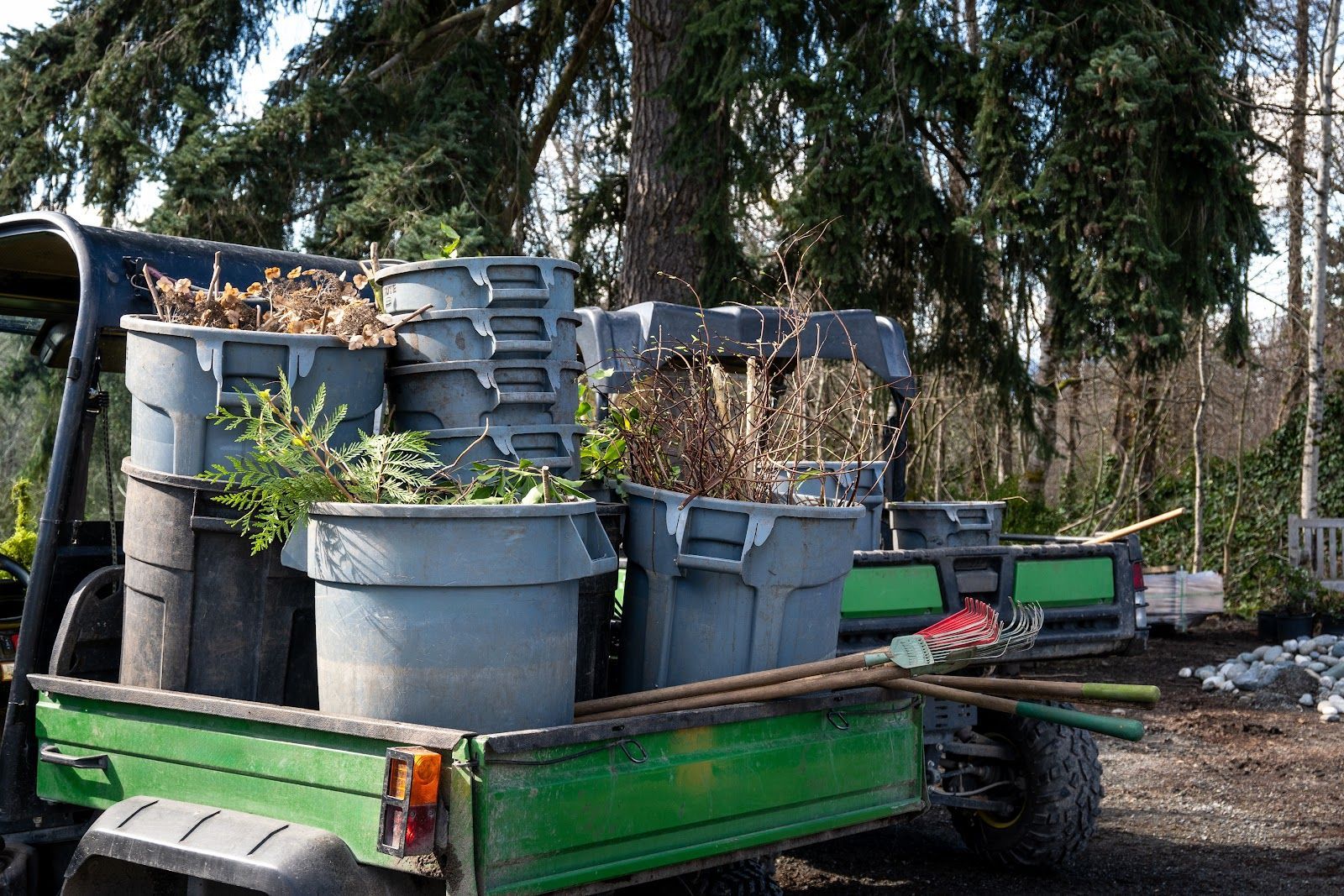 Green utility vehicle loaded with gray bins of yard waste and tools.